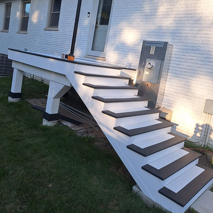 Escaleras exteriores que conducen a la puerta lateral de un edificio de ladrillo blanco, ubicadas de forma incómoda sobre un contador de servicios públicos. La escena indica un descuido de diseño.